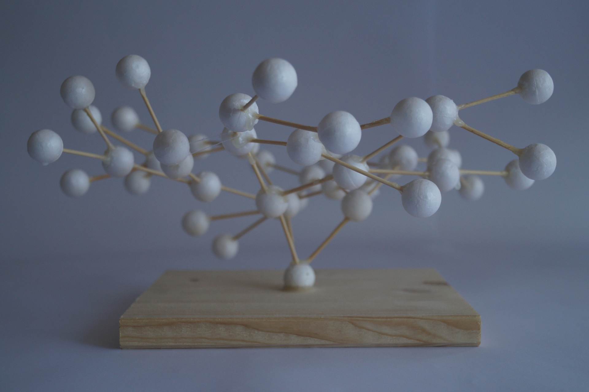 A tree made from styrofoam balls, connected with toothpicks and held in place by thin coards on a base of wood.