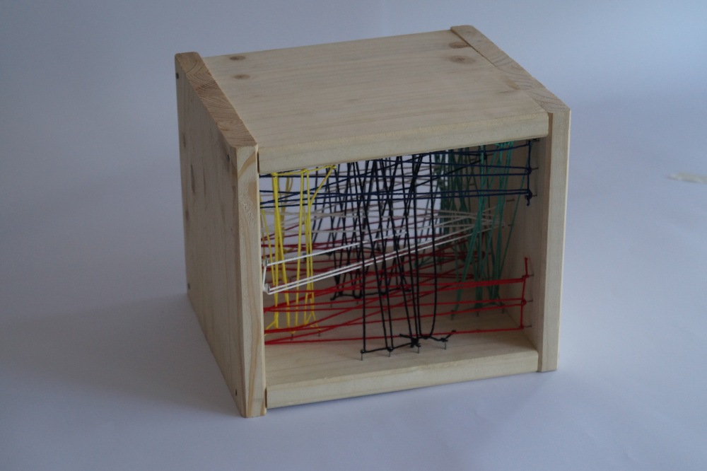 A wooden cube with the front and back missing. Inside is a series of strings that either alternate from the top to the bottom plate or from the left to the right plate. Each series has its own distinct color.