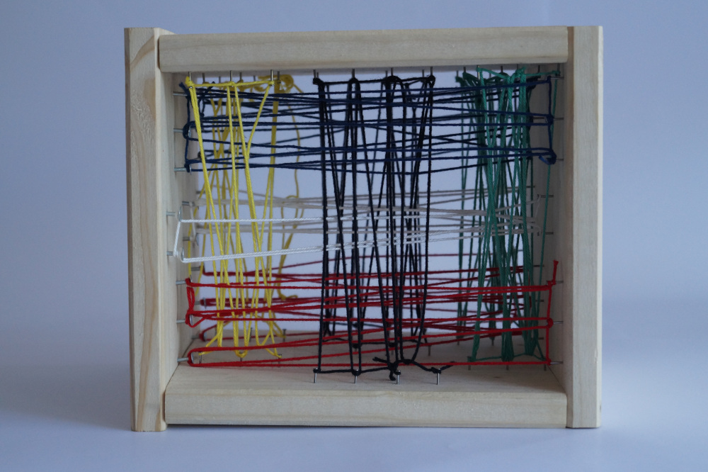 A wooden cube with the front and back missing. Inside is a series of strings that either alternate from the top to the bottom plate or from the left to the right plate. Each series has its own distinct color.